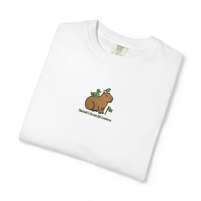 Close-up of a Comfort Colors® white shirt featuring an embroidered brown capybara with two green birds and the saying “Huzzah! I Accept All Creatures.”
