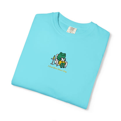  Close-up of a Lagoon Blue Comfort Colors® shirt featuring a cozy green frog reading in an armchair by candlelight with the saying “I Read While Others Sleep.