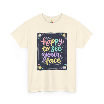 Close-up of a Light BEIGE T-shirt featuring a colorful "Happy to See Your Face" hand-lettered graphic framed with flowers and hearts on a navy background panel.
