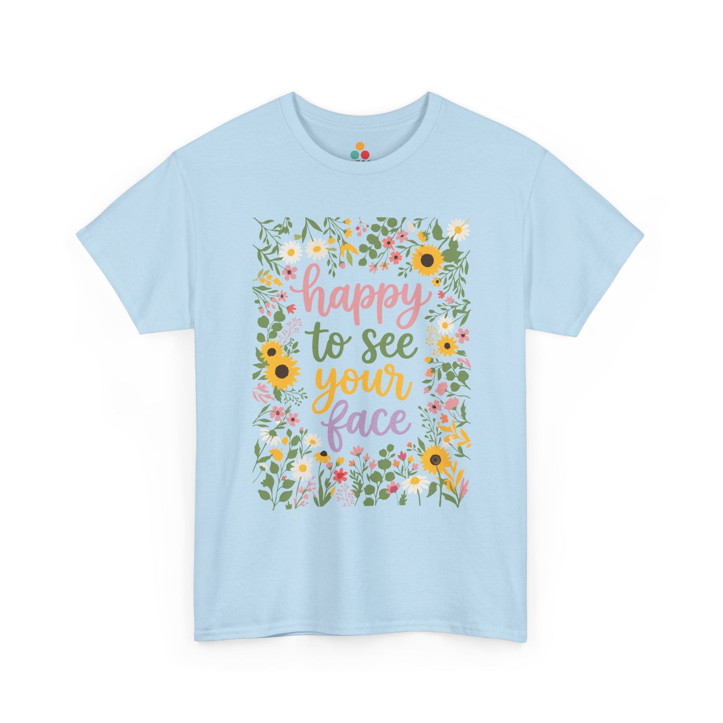 Close-up of a Light Blue T-shirt featuring the phrase “Happy to See Your Face” in pastel lettering framed by a floral border with sunflowers and wildflowers.

