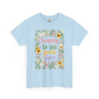 Close-up of a Light Blue T-shirt featuring the phrase “Happy to See Your Face” in pastel lettering framed by a floral border with sunflowers and wildflowers.

