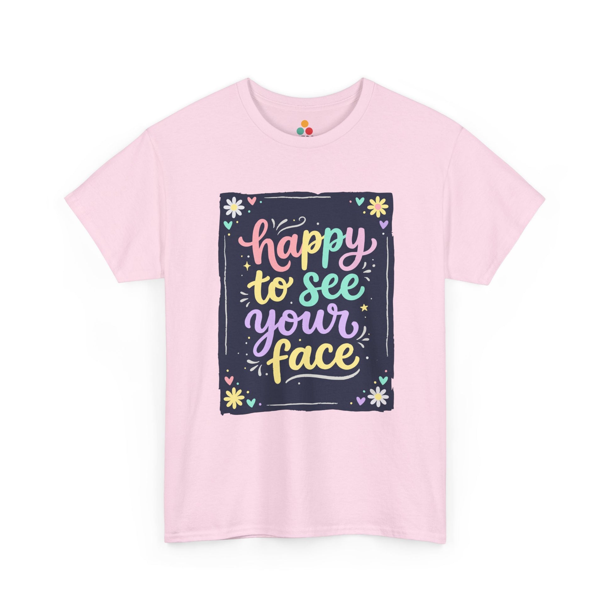 Close-up of a Light Pink T-shirt featuring a colorful "Happy to See Your Face" hand-lettered graphic framed with flowers and hearts on a navy background panel.
