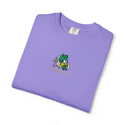  Close-up of a Violet Comfort Colors® shirt featuring a cozy green frog reading in an armchair by candlelight with the saying “I Read While Others Sleep.