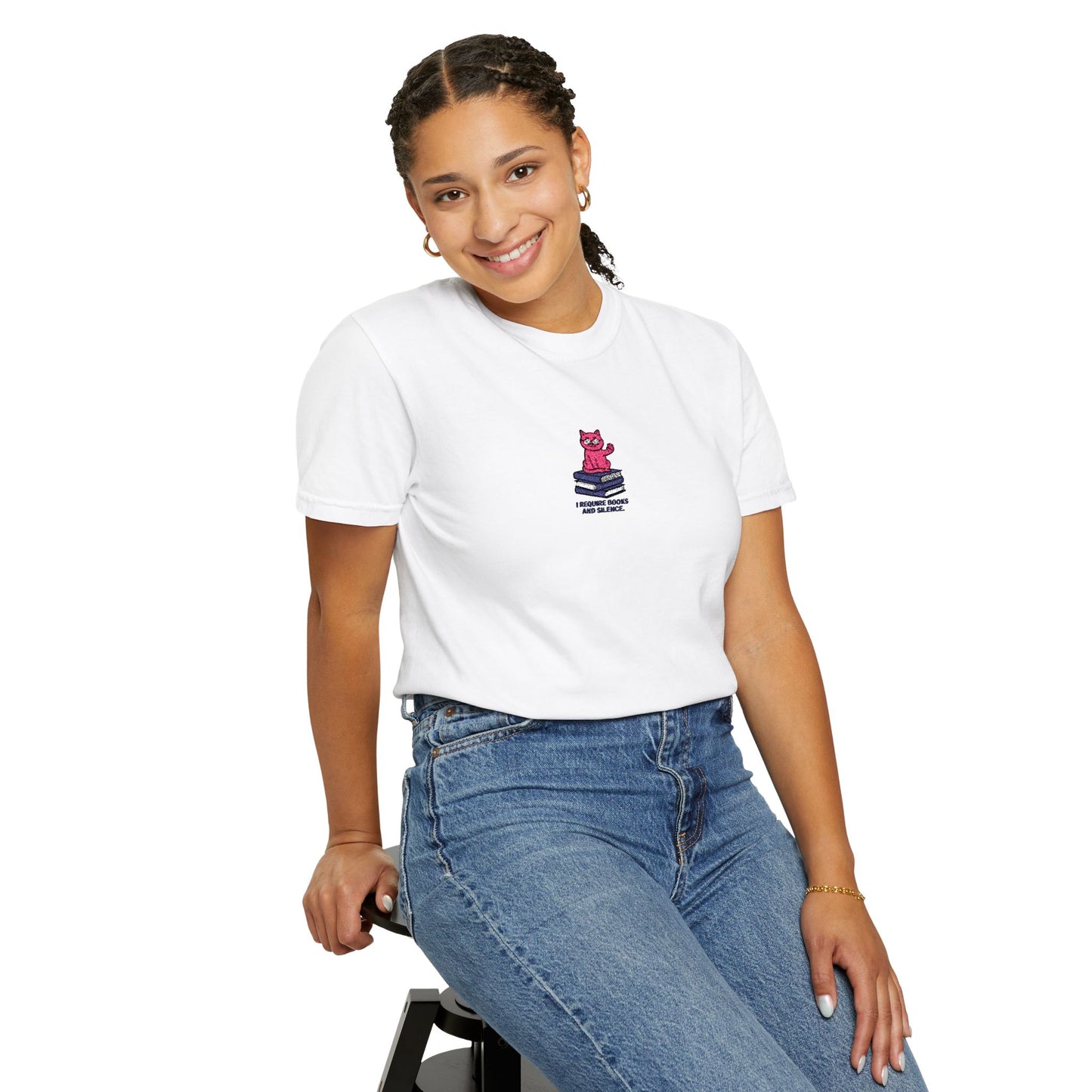   Close-up of a female model wearing Comfort Colors®  white shirt featuring an embroidered pink cat sitting on books with the saying “I Require Books and Silence.”


