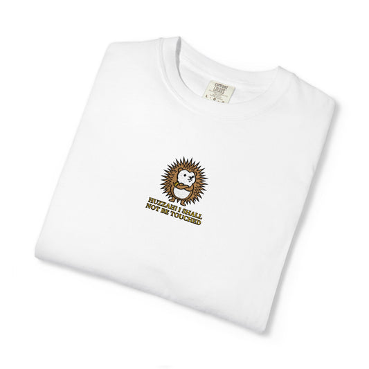 Close-up of a white Comfort Colors® shirt featuring an embroidered round hedgehog with gold text saying "Huzzah! I Shall Not Be Touched."

