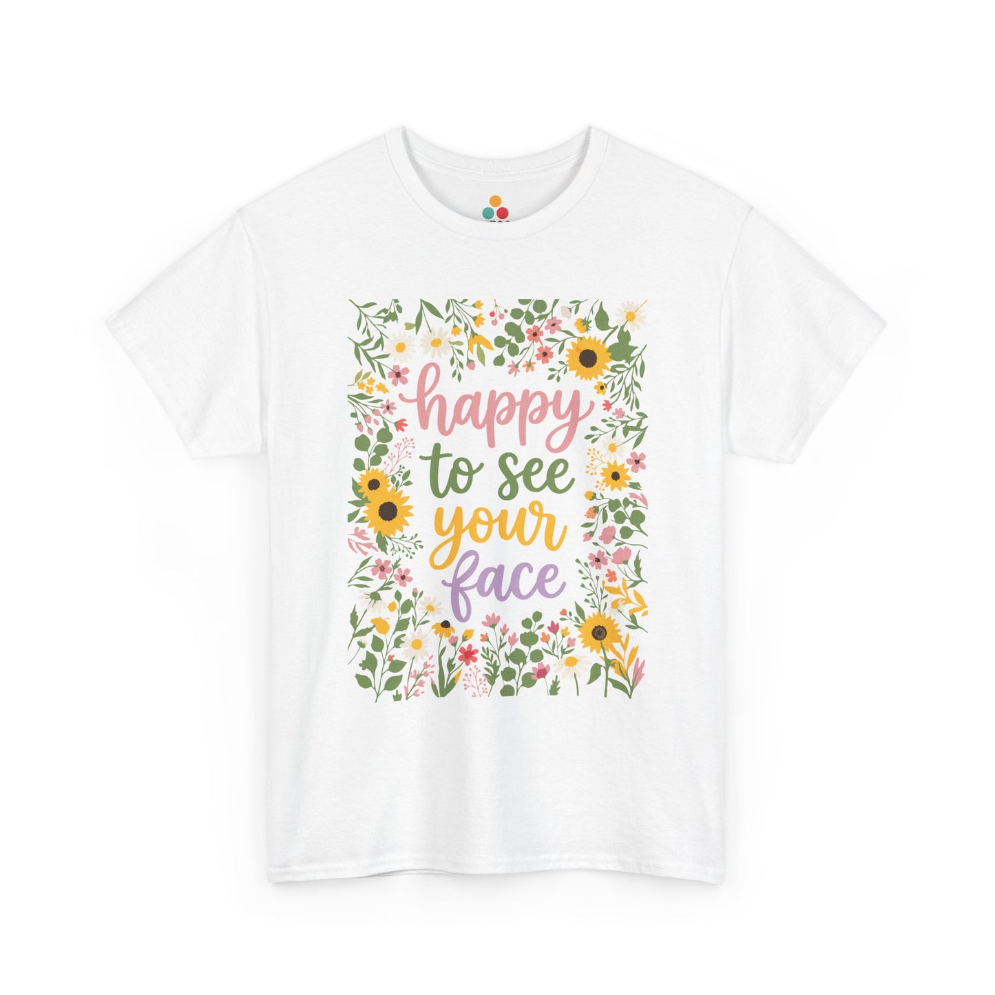 Close-up of a white T-shirt featuring the phrase “Happy to See Your Face” in pastel lettering framed by a floral border with sunflowers and wildflowers.
