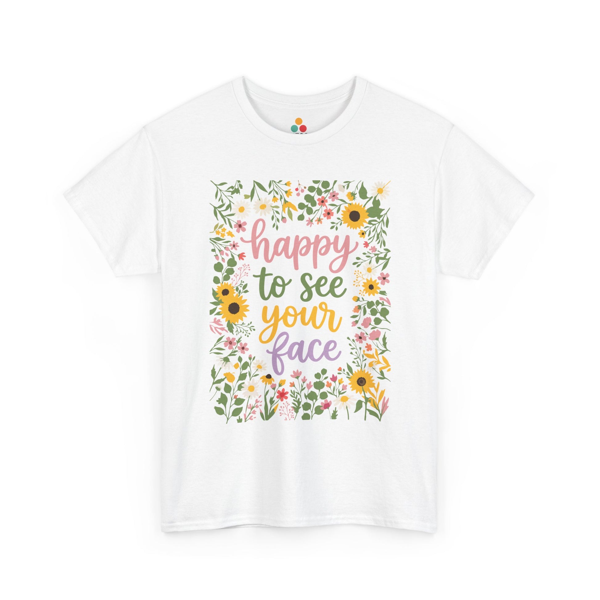 Close-up of a white T-shirt featuring the phrase “Happy to See Your Face” in pastel lettering framed by a floral border with sunflowers and wildflowers.
