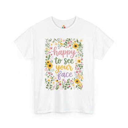 Close-up of a white T-shirt featuring the phrase “Happy to See Your Face” in pastel lettering framed by a floral border with sunflowers and wildflowers.
