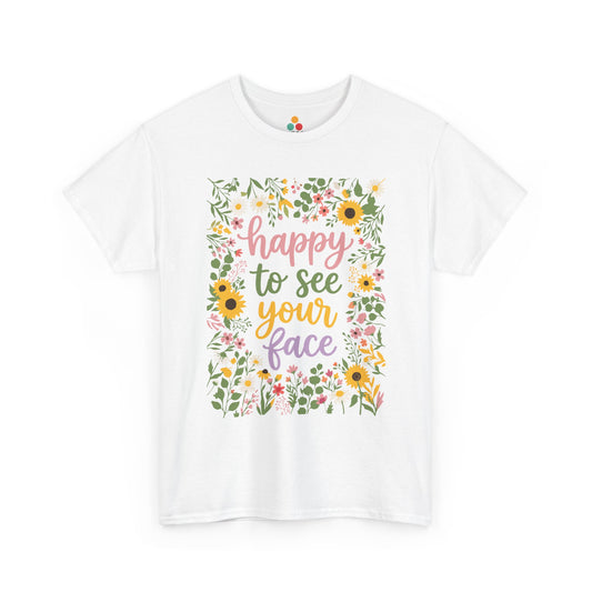 Close-up of a white T-shirt featuring the phrase “Happy to See Your Face” in pastel lettering framed by a floral border with sunflowers and wildflowers.
