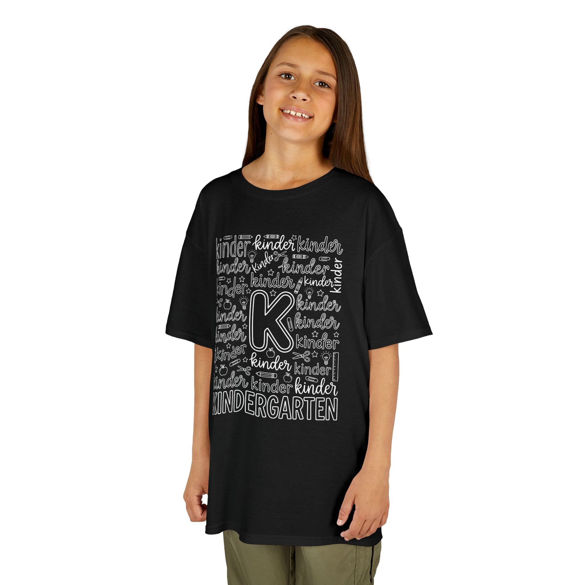 Girl wearing a black TEEZOCA kindergarten typography kids tee reading kindergarten, a cute first-day-of-school shirt.

