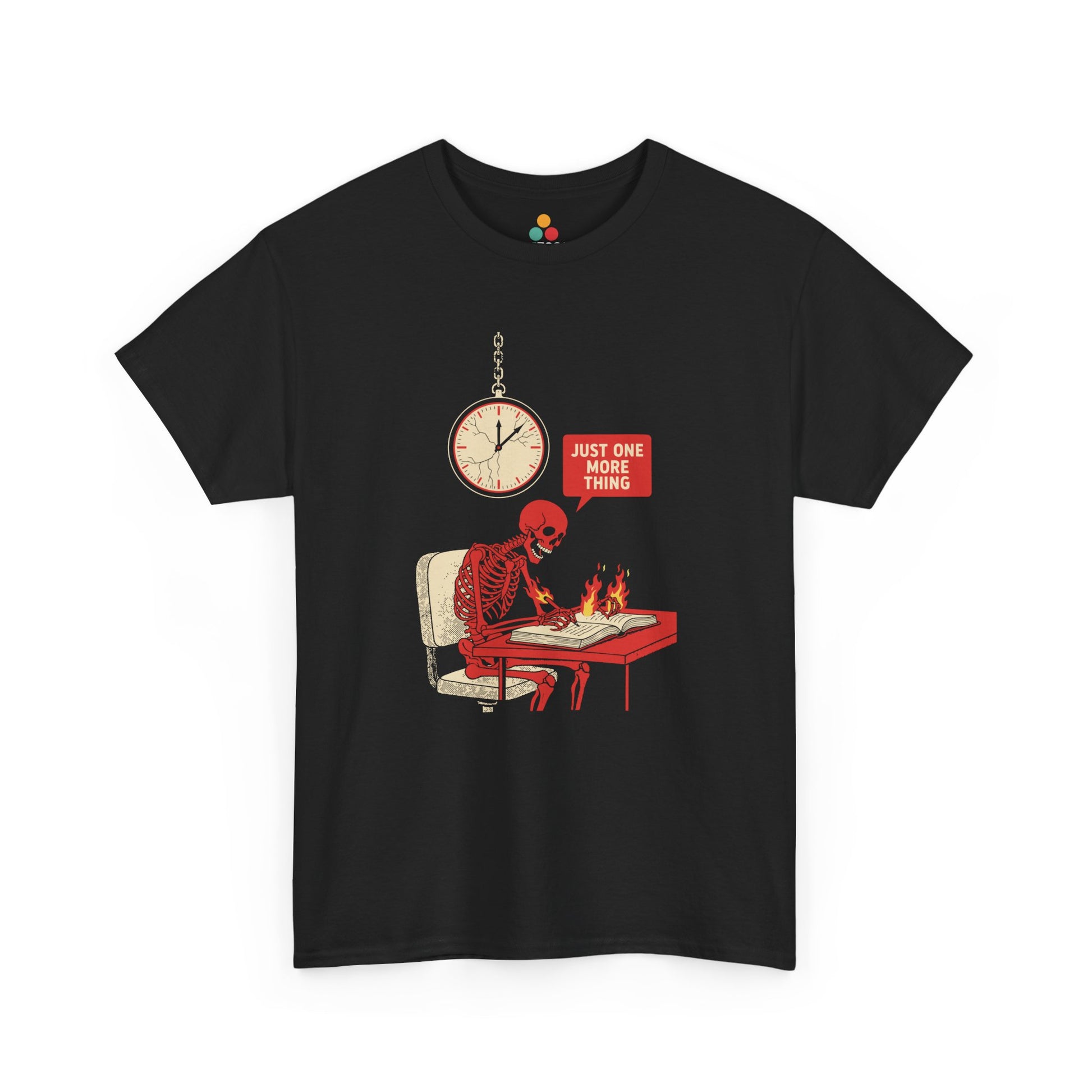Graphic t‑shirt featuring a red skeleton sitting at a desk with hands on fire, writing in a book under a wall clock, with a speech bubble saying “Just One More Thing.”
