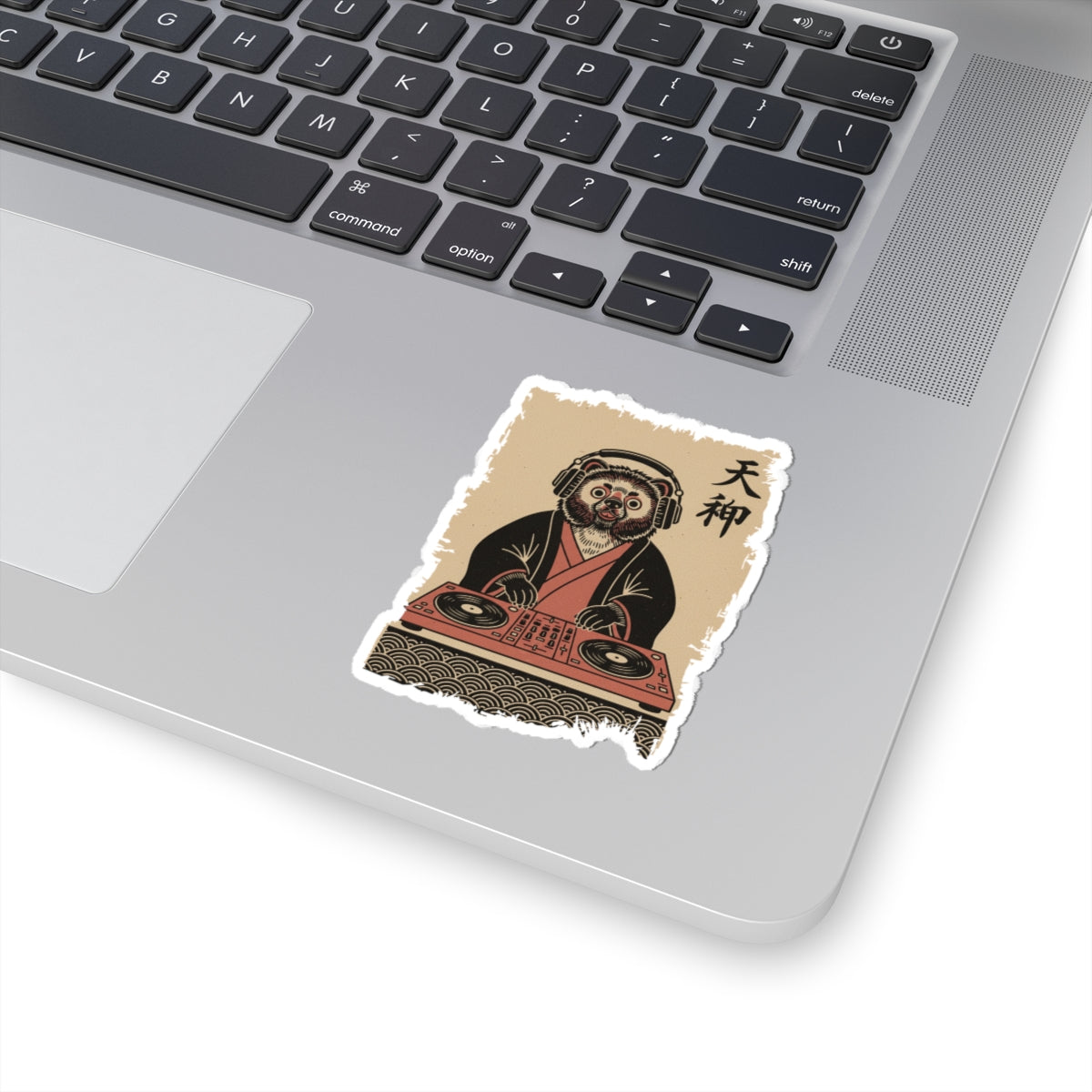 Laptop with a sticker of a person in traditional attire using DJ equipment on the palm rest area.