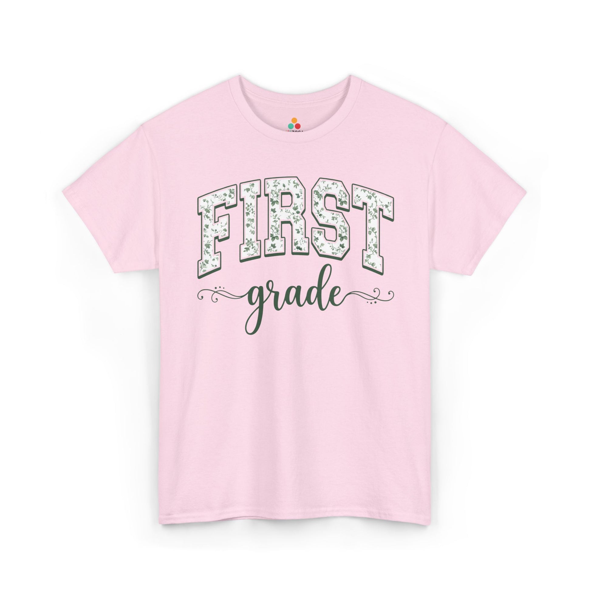 Pink t-shirt with 'FIRST grade' text on a white background. TEEZOCA first grade teacher shirt featuring sage floral varsity lettering, a cute back to school tee for teachers.
