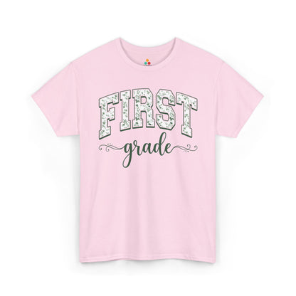 Pink t-shirt with 'FIRST grade' text on a white background. TEEZOCA first grade teacher shirt featuring sage floral varsity lettering, a cute back to school tee for teachers.
