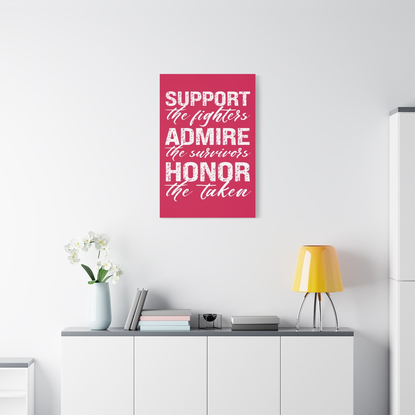 TEEZOCA “Support the fighters admire the survivors honor the taken” canvas hanging above a couch with yellow lamp.