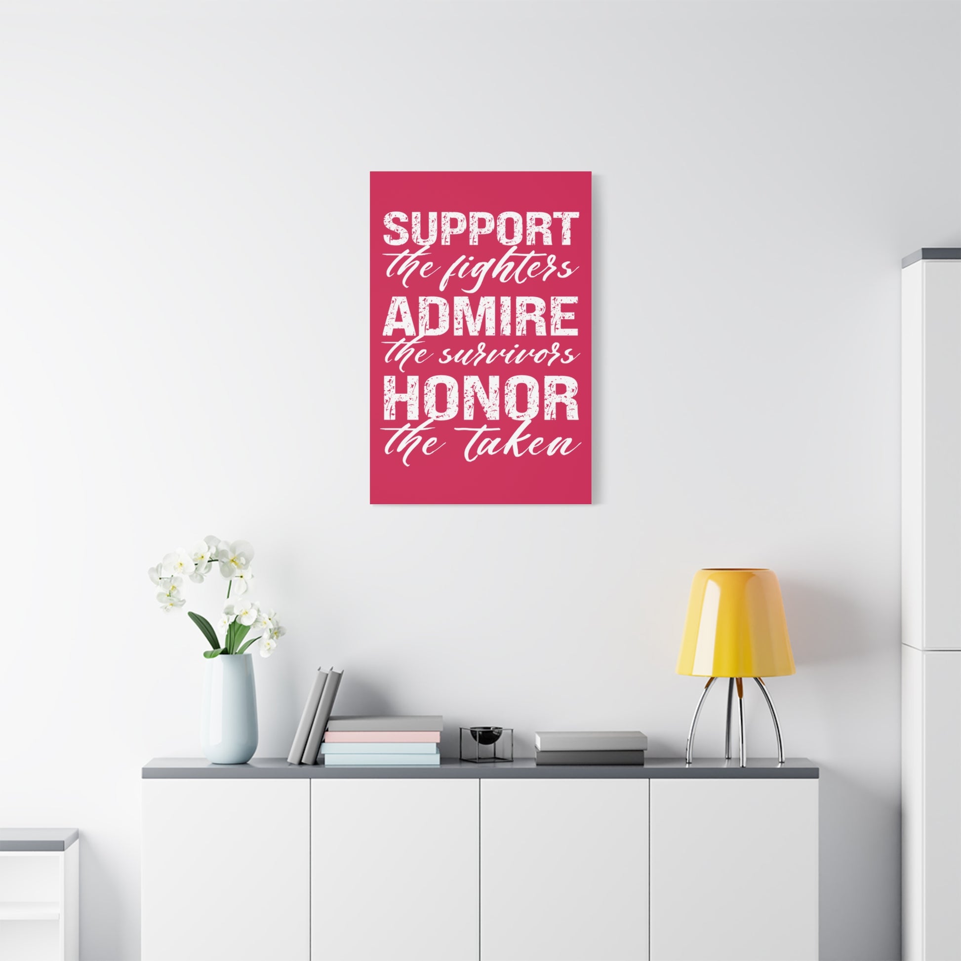 TEEZOCA “Support the fighters admire the survivors honor the taken” canvas hanging above a couch with yellow lamp.