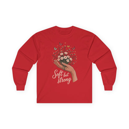 TEEZOCA soft but strong floral artwork on unisex long-sleeve t-shirt Red long-sleeve shirt with a graphic of a hand holding flowers and text 'Soft but Strong' on a white background.