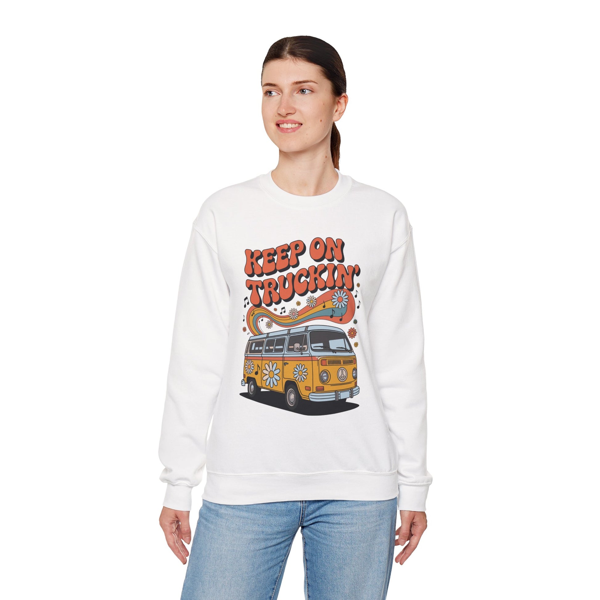 TEEZOCA unisex sweatshirt featuring a retro van with daisies, rainbow waves, music notes, and “Keep On Truckin’” vintage typography Woman wearing a white sweatshirt with a graphic design of a van and text on a white background