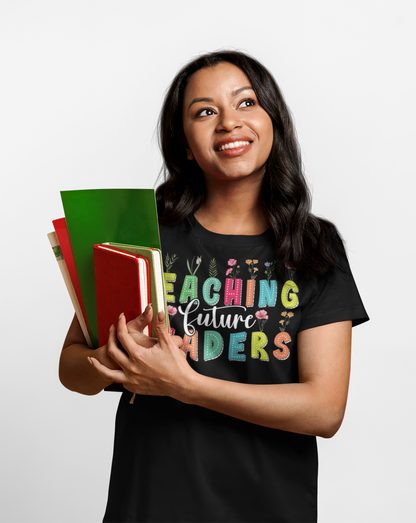 Woman Teacher holding books and wearing a black t-shirt with 'Teaching Future Leaders' text.
