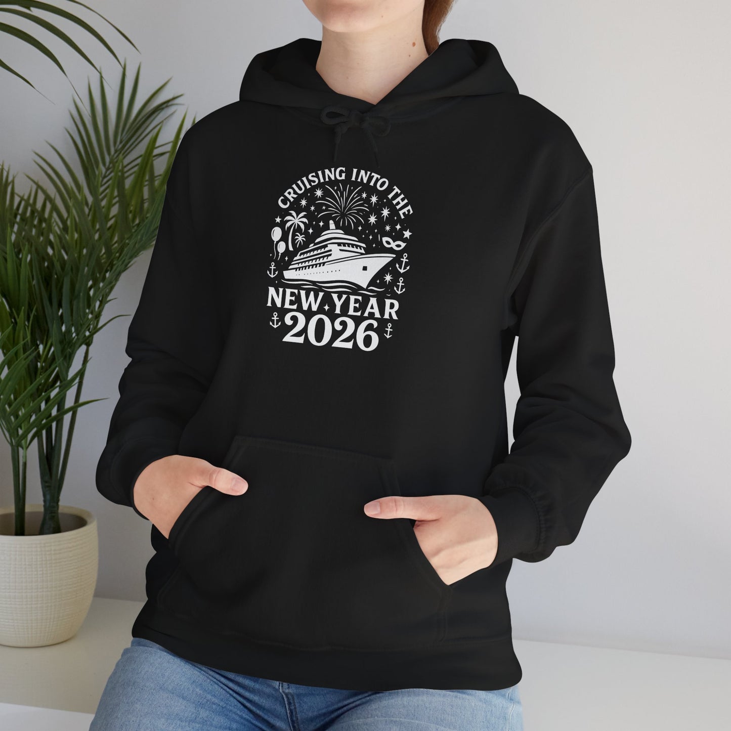 Person sitting indoors wearing black New Year 2026 cruise ship hoodie with hands in pocket, lifestyle mockup.