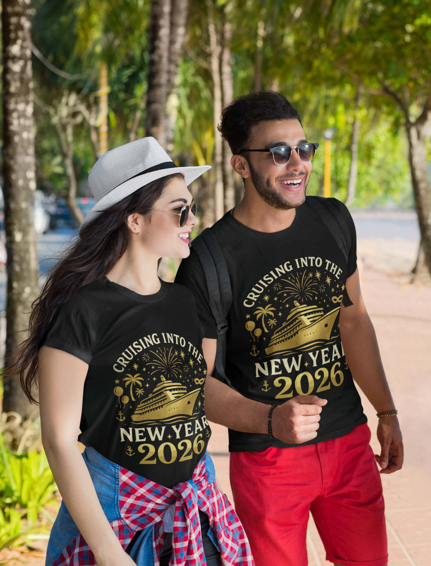 Couple wearing matching black “Cruising Into The New Year 2026” gold cruise ship T-shirts while walking outdoors, lifestyle photo.