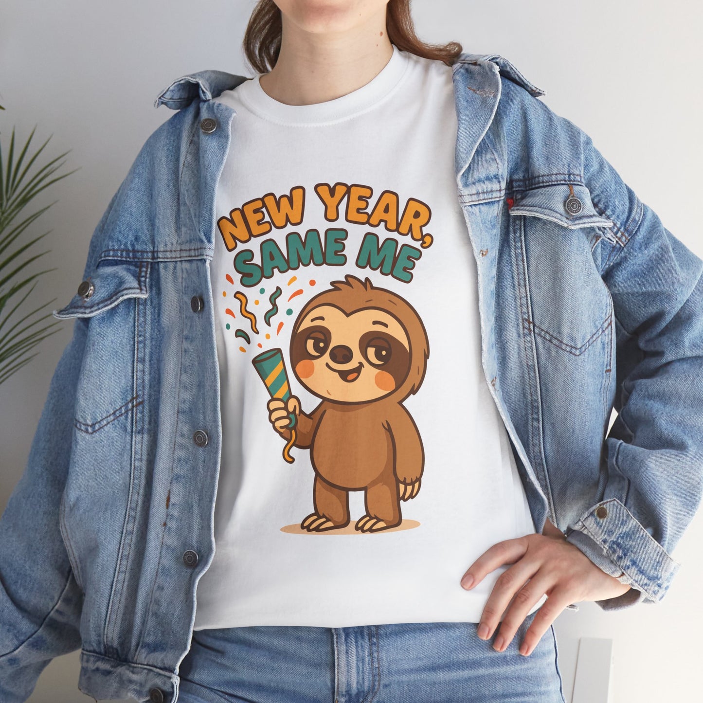 Woman wearing white “New Year Same Me” sloth T-shirt under a denim jacket, seated and smiling, lifestyle photo.