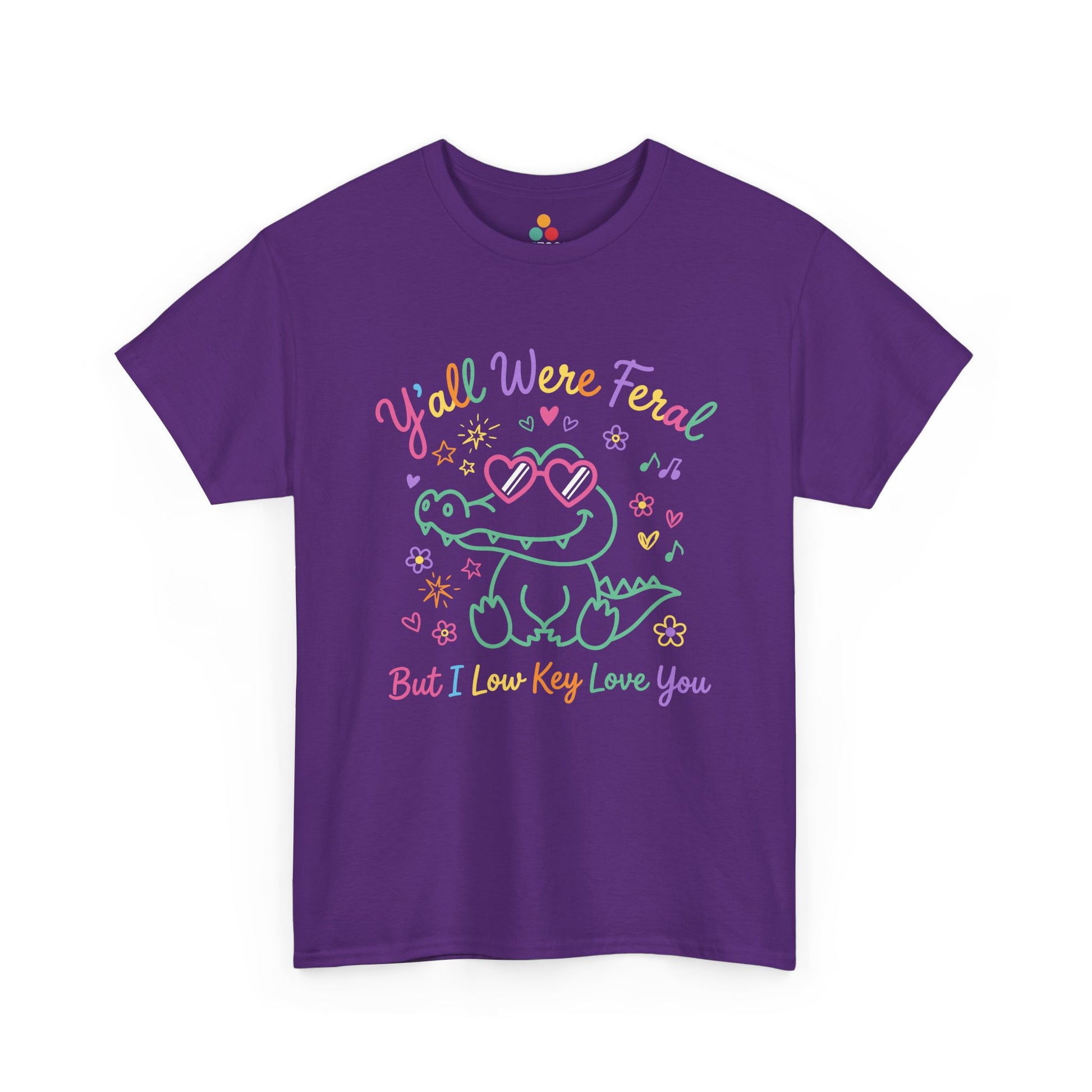 purple t-shirt  crocodile wearing heart-shaped sunglasses surrounded by colorful stars and flowers, with rainbow text reading "Y'all Were Feral But I Low Key Love You" — a funny last day of school teacher gift shirt.

