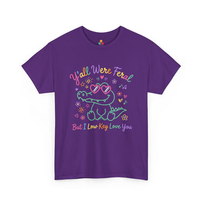purple t-shirt  crocodile wearing heart-shaped sunglasses surrounded by colorful stars and flowers, with rainbow text reading "Y'all Were Feral But I Low Key Love You" — a funny last day of school teacher gift shirt.

