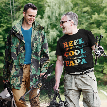 Two men outdoors wearing matching “Reel Cool Papa” fishing T‑shirts, standing with fishing gear, lifestyle photo.